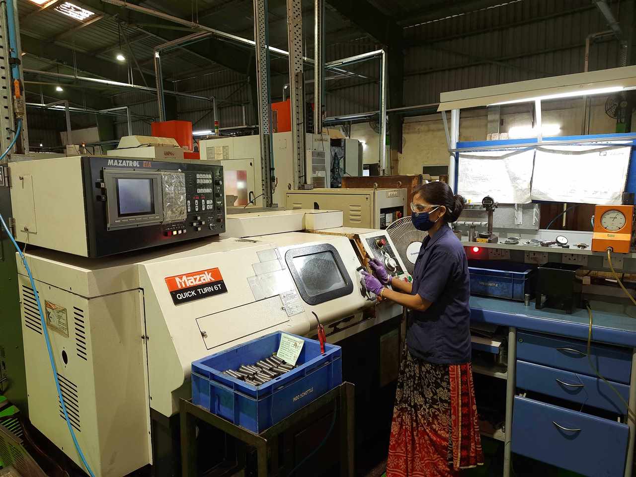 A PSCPL machinist working at a single-spindle CNC turning centre, with a tray of finished shafts beside the machine