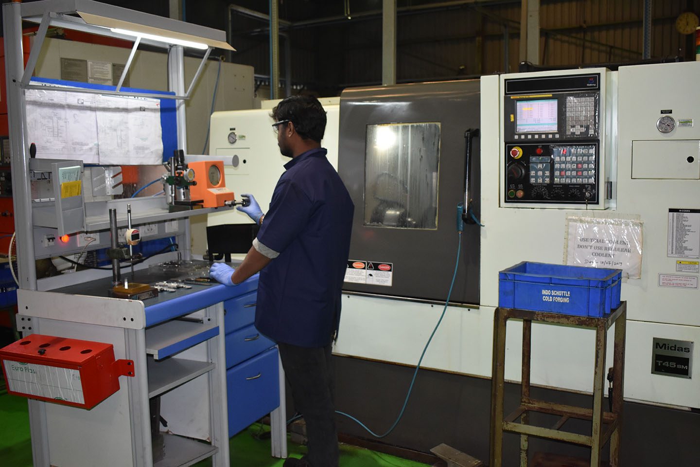 A machinist gauging a part at the inspection bench beside a turn-mill centre on the PSCPL shop floor